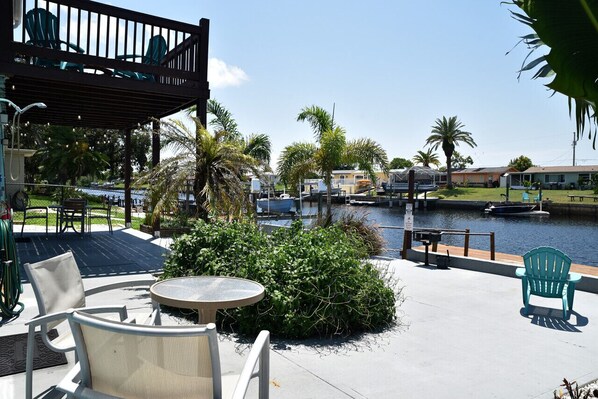 An outdoor patio with chairs and a table, overlooking a body of water with boats and houses in the background. - SF Hudson oh beautiful Hudson (Hudson)