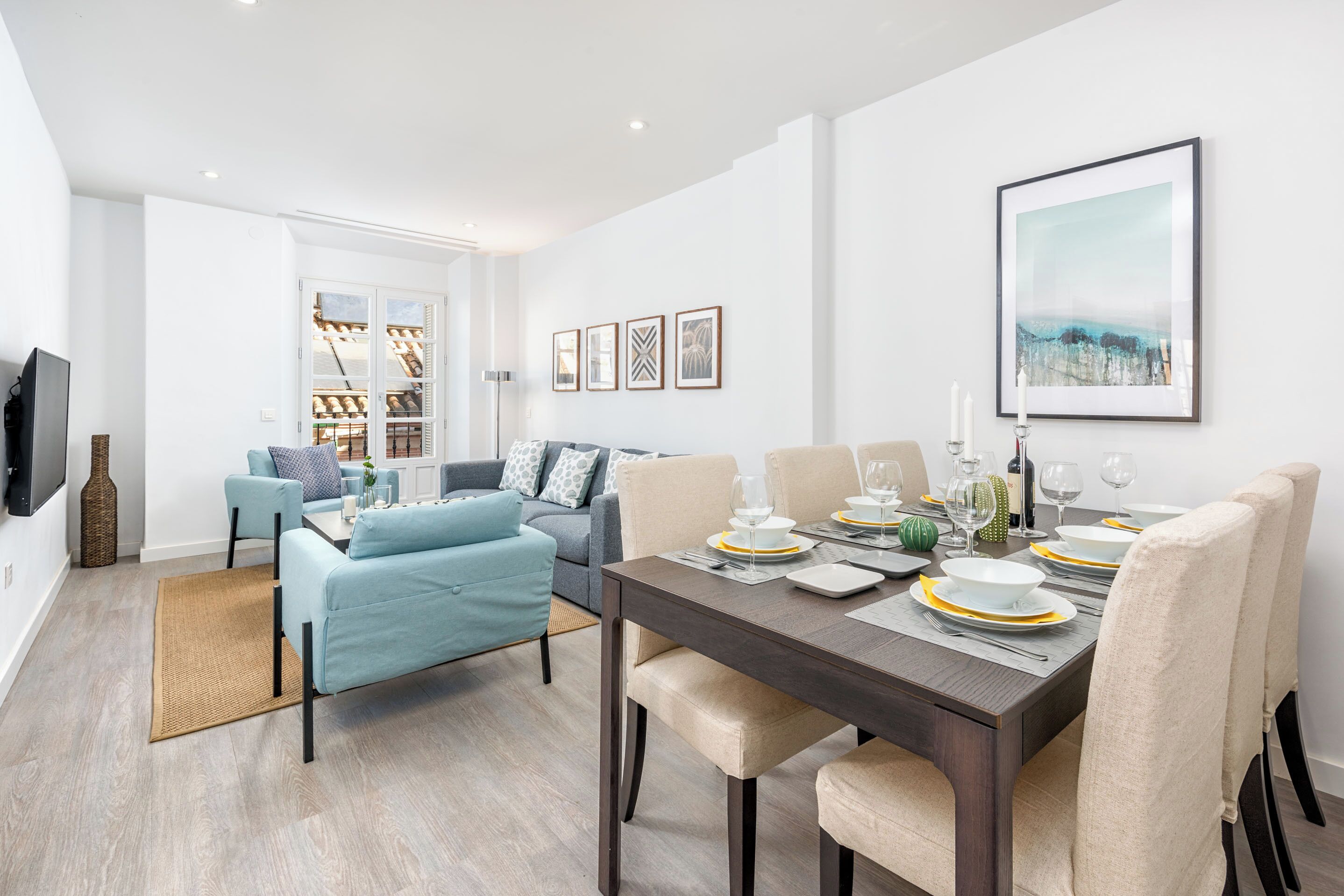 Una sala de estar moderna con comedor, que incluye un sofá, una mesa de comedor para cuatro personas y un televisor de pantalla plana montado en la pared.