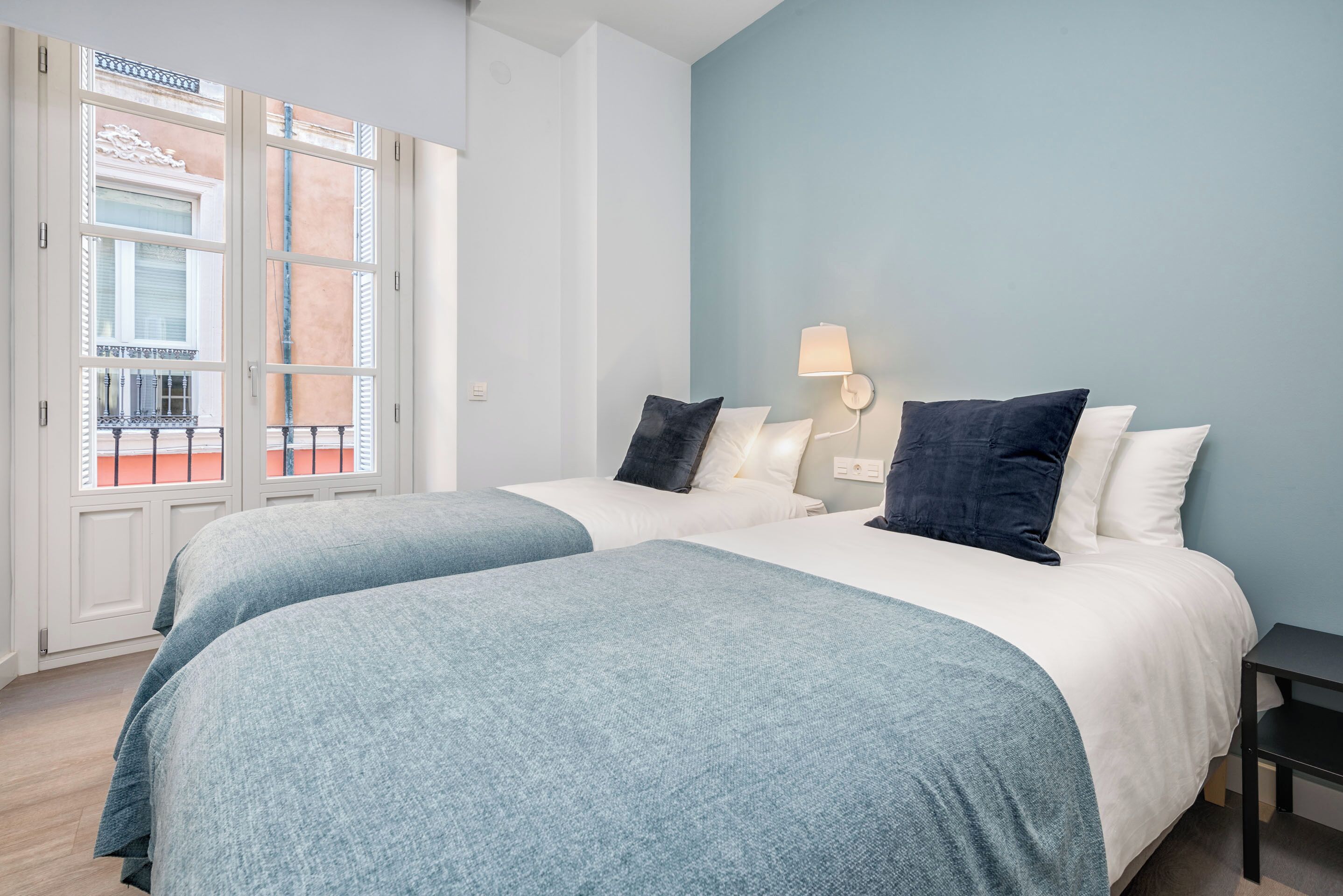 A hotel room with two beds, a balcony, and a light blue wall.