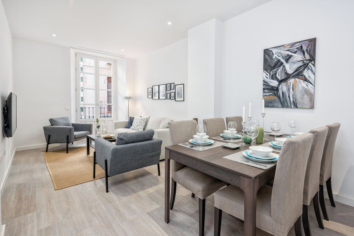 A modern dining area with a wooden table set for four, surrounded by grey upholstered chairs.