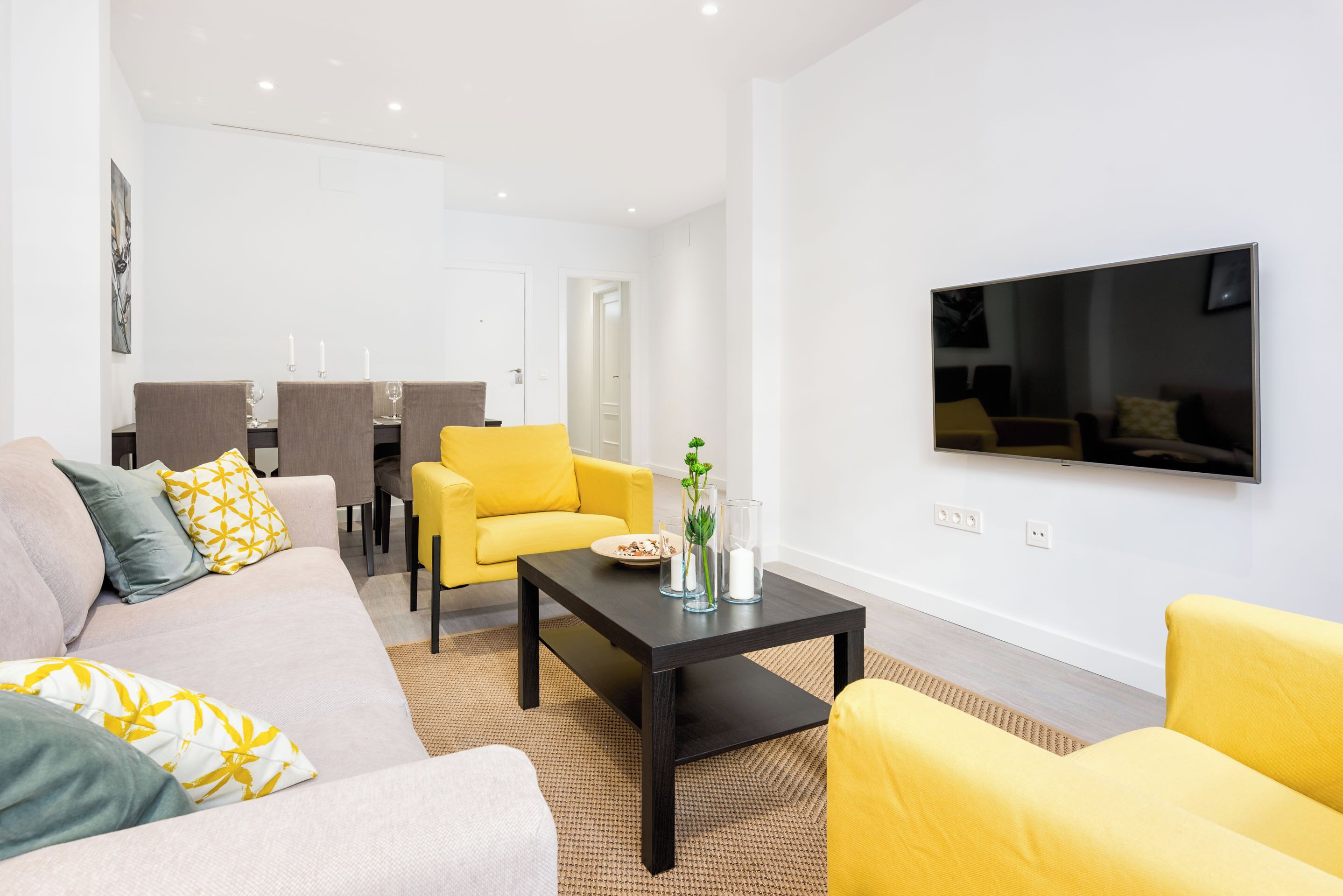Ein modernes Wohnzimmer mit einer Couch, gelben Sessel, einem Couchtisch und einem flachbildfernseher an der Wand.