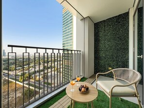 Enjoy a city view from this balcony with a table for two, wicker chair, and artificial grass floor.