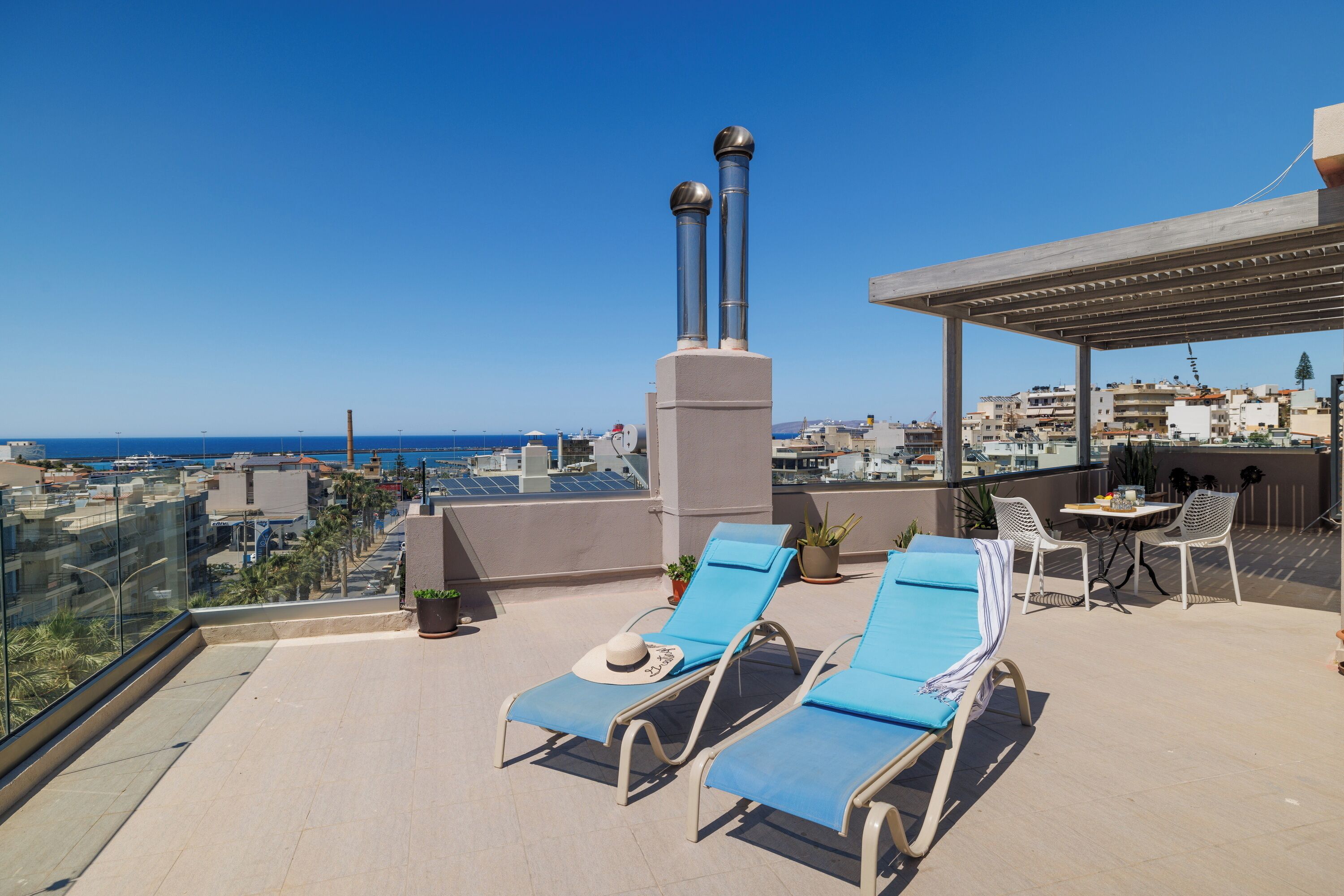 A rooftop terrace with lounge chairs, a table, and potted plants.