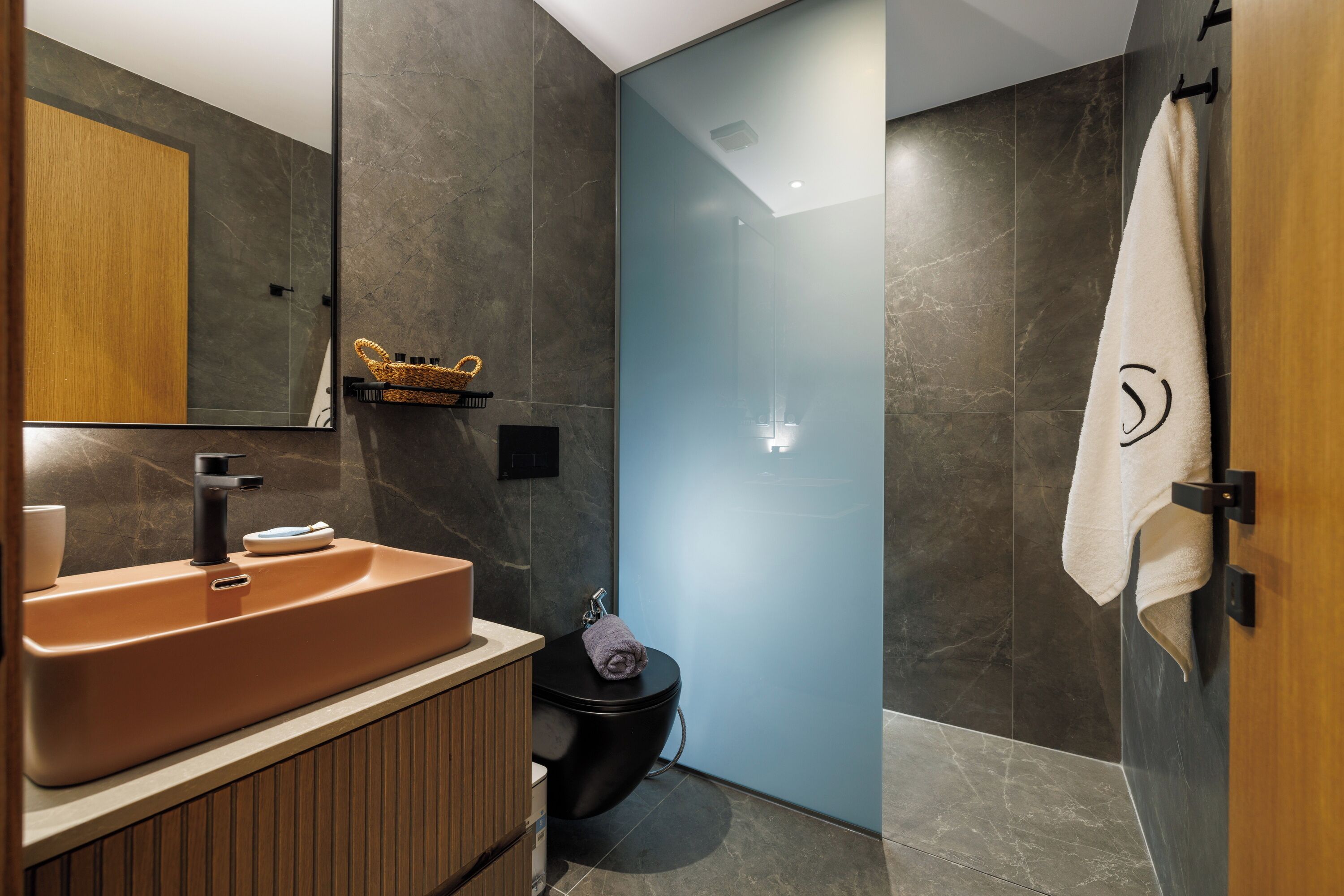 Un baño moderno con tocador de madera, inodoro negro y cabina de ducha de vidrio.