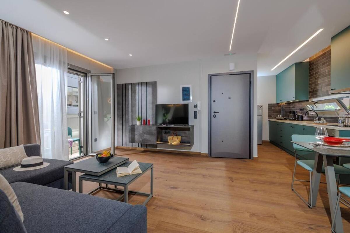 Ein modernes Wohnzimmer mit einer Couch, einem Couchtisch und einem Fernseher. Es gibt eine Küchenzeile mit einem Esstisch und Stühlen.