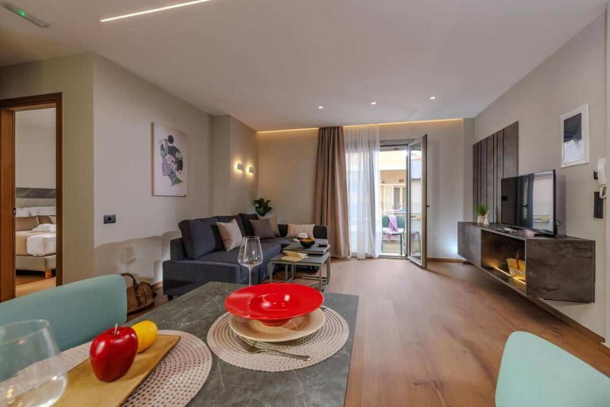 Ein modernes Wohnzimmer mit einer Couch, einem Esstisch mit rotem Teller und einem Fernseher an einer Wandhalterung.