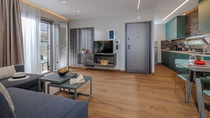 A modern living room with a sofa, a small table, and a TV. There is a kitchen area with a dining table and chairs. - Jolly Suites (Heraklion)