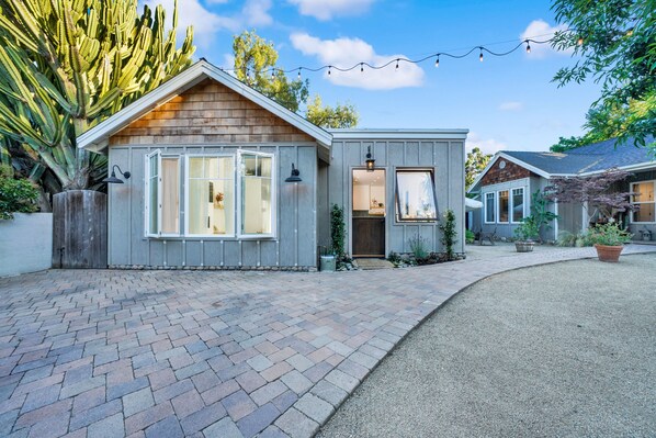 Une petite maison de plain-pied avec une allée en briques, un revêtement en bois et un petit porche.