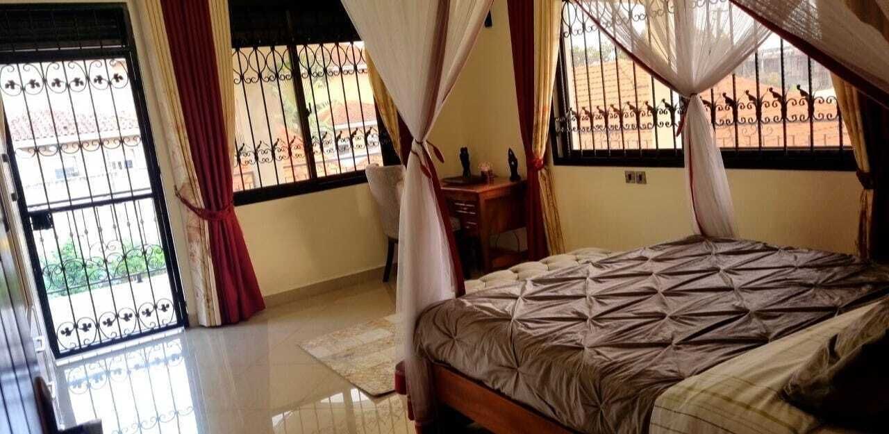 A bedroom with a bed, curtains, a desk, and a window with metal bars.