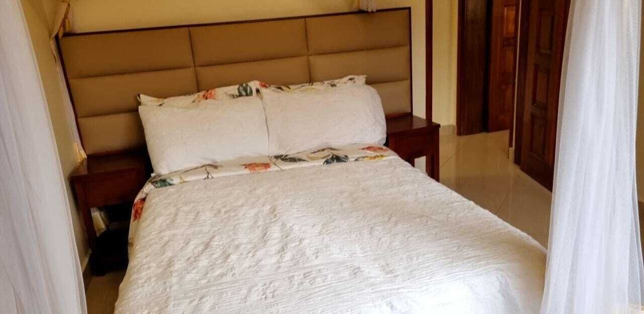 A neatly made bed with a floral-patterned bedspread and two pillows, a wooden headboard, and a wooden nightstand with a lamp.