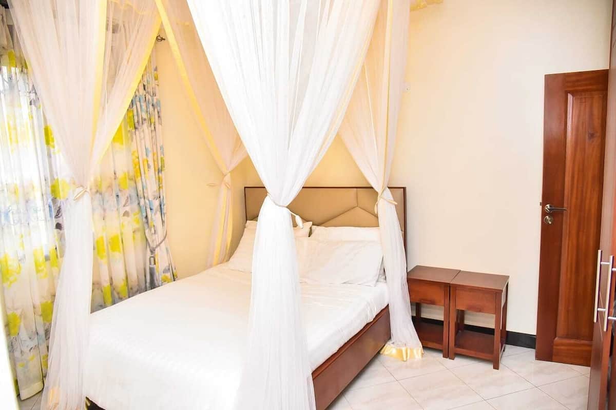 A bedroom with a bed, a nightstand, a wooden door, and a curtain with a floral pattern.