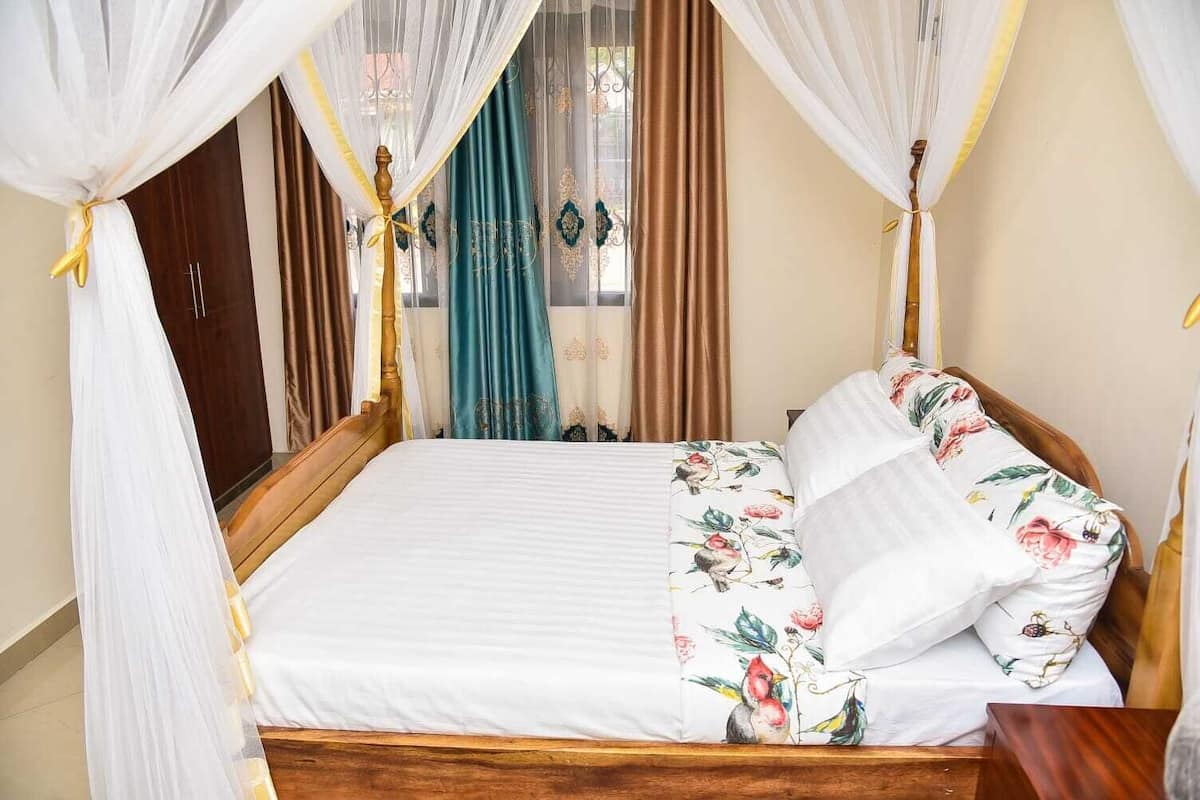 A bed with a floral bedspread, a wooden headboard, and a canopy with white and yellow drapes.