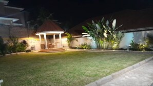 A well-lit gazebo with a tiled floor, surrounded by a manicured lawn and various plants. - KCube Villas Kampala (Kampala)
