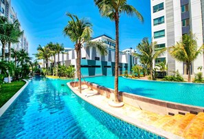 A swimming pool with palm trees and modern buildings in the background. - 2-bedroom condo in delightful Muang Pattaya with AC, WiFi, fitness room (Muang Pattaya)