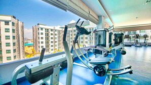 A gym with exercise equipment and a view of high-rise buildings. - 2-bedroom condo in delightful Muang Pattaya with AC, WiFi, fitness room (Muang Pattaya)