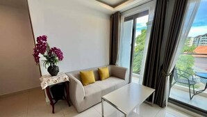 A modern living room with a sofa, a coffee table, and a small side table with a vase of flowers. - 2-bedroom condo in delightful Muang Pattaya with AC, WiFi, fitness room (Muang Pattaya)