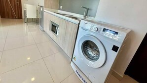 A modern kitchen with a built-in Samsung washing machine, wooden cabinets, and a white countertop. - 2-bedroom condo in delightful Muang Pattaya with AC, WiFi, fitness room (Muang Pattaya)