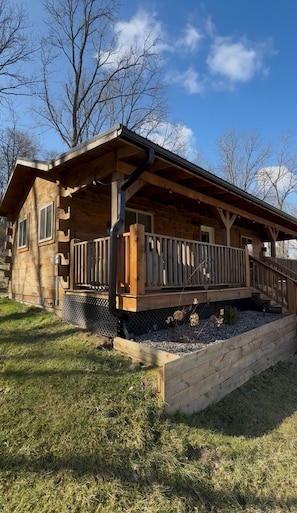 Eine Holzhütte mit Veranda, einer kleinen Terrasse und einem erhöhten Blumenbeet.