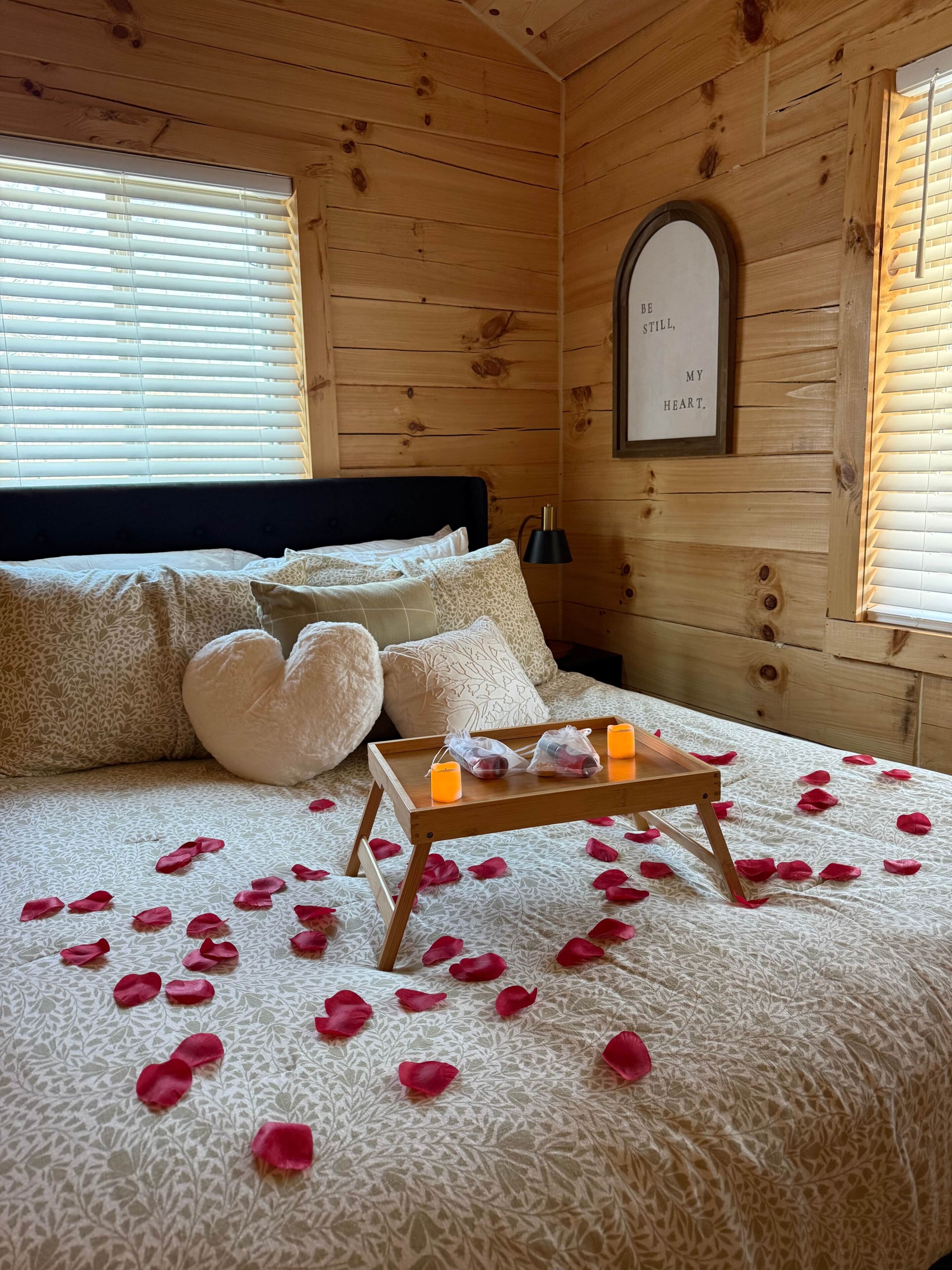 Une chambre à coucher dans un chalet en bois, avec un lit, des oreillers, une table de chevet avec des bougies et une citation encadrée accrochée au mur.