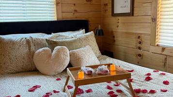 Une chambre à coucher dans un chalet en bois, avec un lit, des oreillers, une table de chevet avec des bougies et une citation encadrée accrochée au mur.