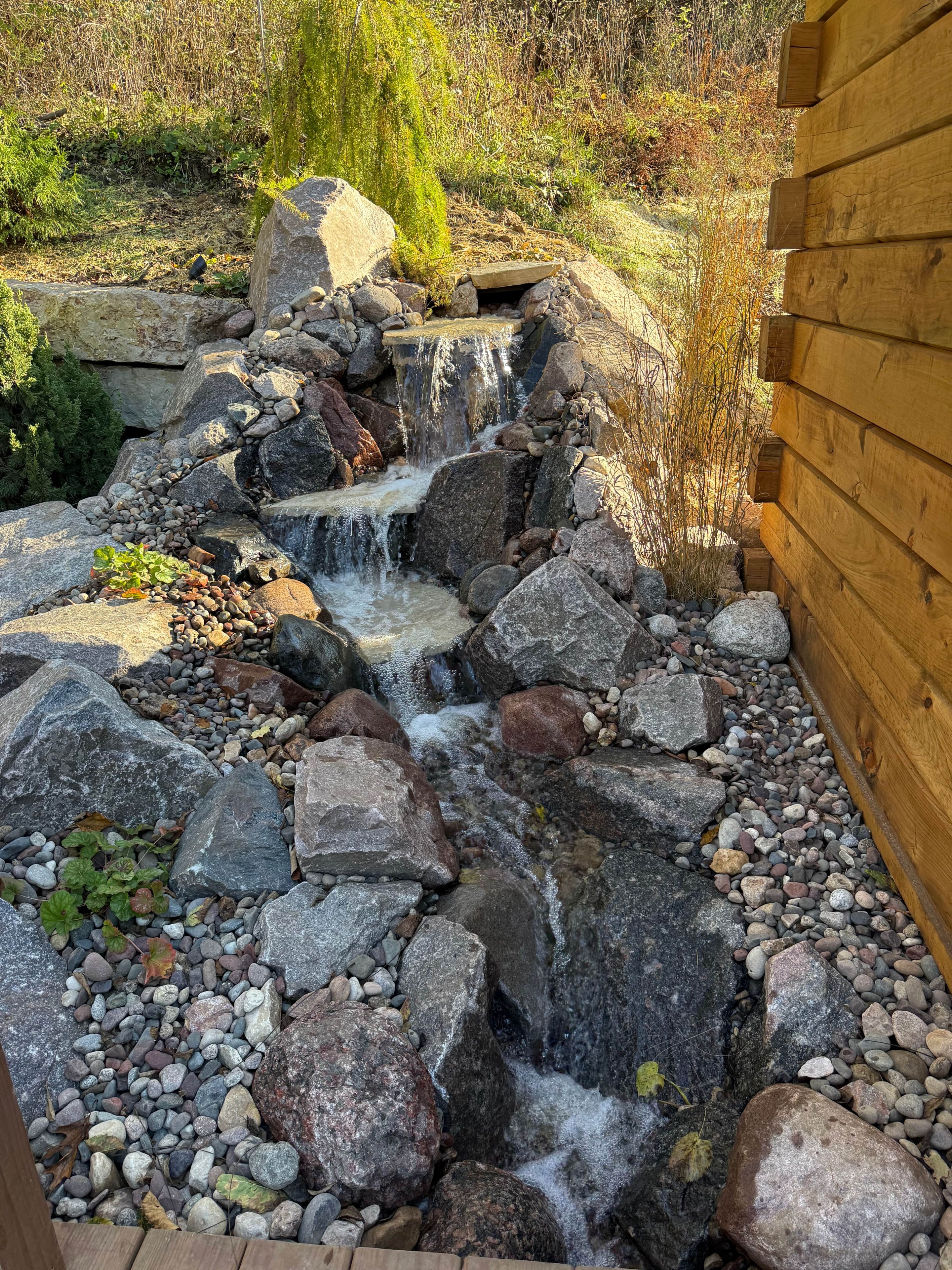 Une petite cascade artificielle, entourée de rochers et de végétation.