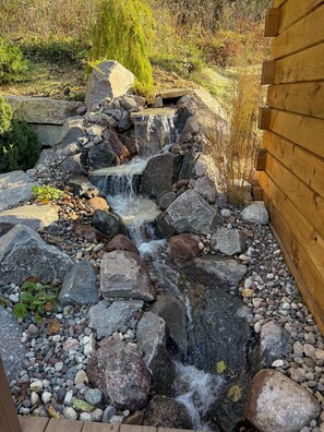 A small waterfall feature surrounded by rocks and vegetation. - Shalom Spa Cabin | Hot Tub, Sauna + Cold Plunge, Shalom Cabin (Gays Mills)