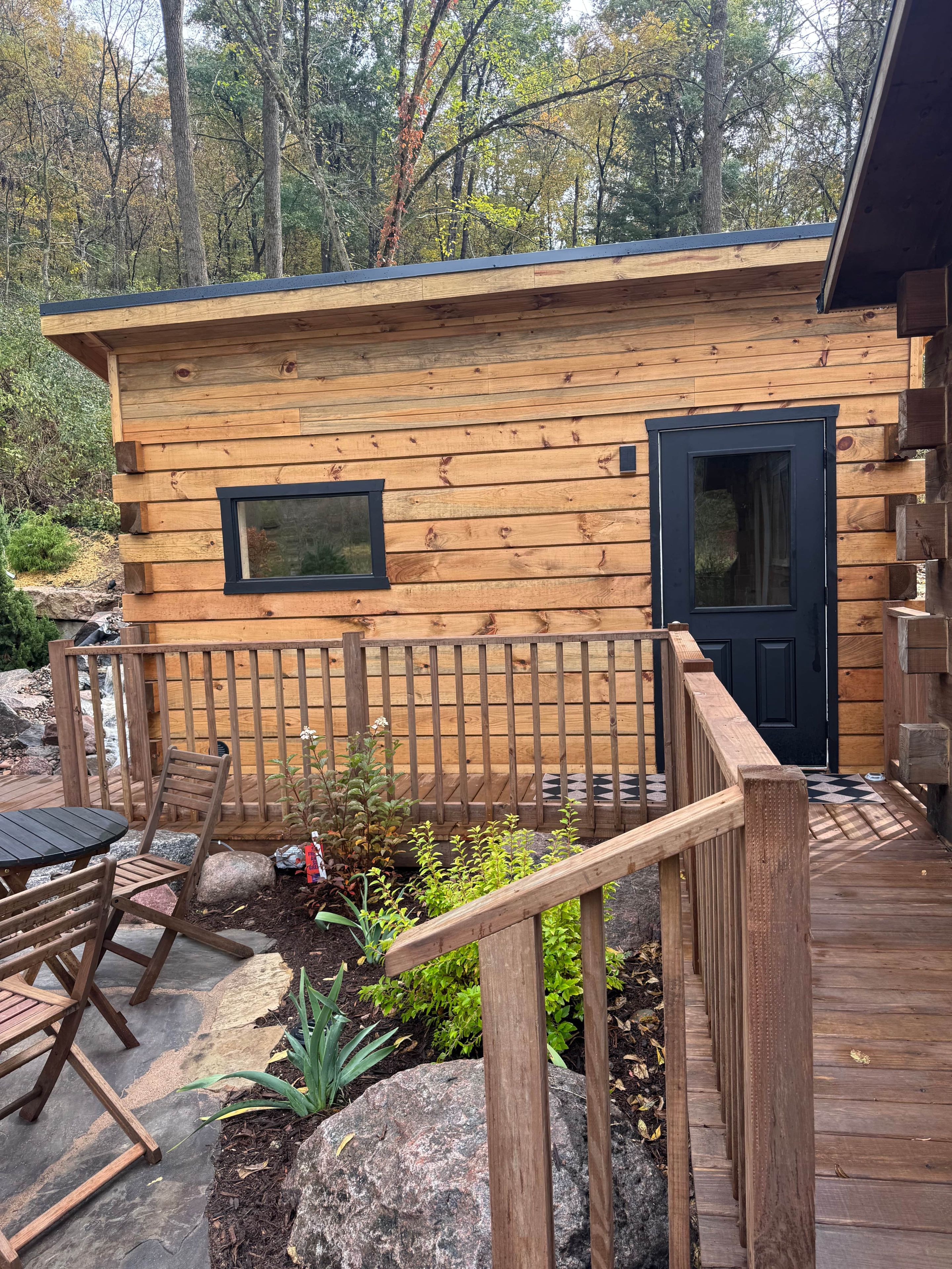 Eine Holzhütte mit einer Terrasse, einer Tür und einem Fenster.