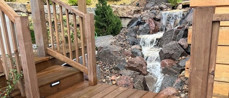 Un patio in legno con una cascata artificiale, circondato da rocce e vegetazione.