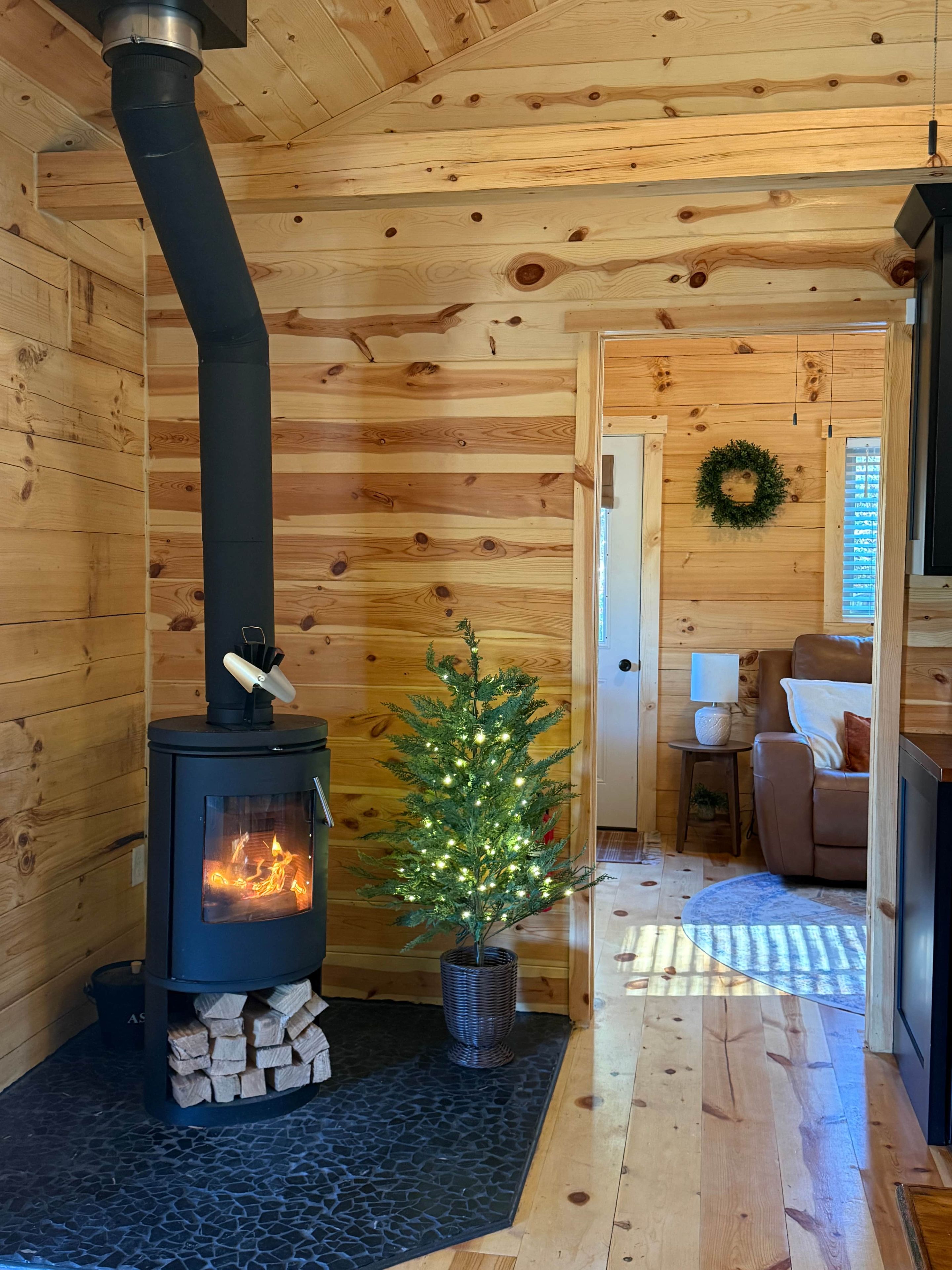 A wood-burning stove with a chimney, a small Christmas tree, and a cozy seating area with a couch and a lamp.