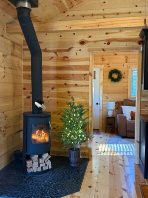A wood-burning stove with a chimney, a small Christmas tree, and a cozy seating area with a couch and a lamp. - Shalom Spa Cabin | Hot Tub, Sauna + Cold Plunge, Shalom Cabin (Gays Mills)
