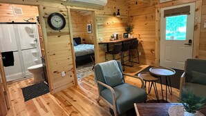 Un intérieur de chalet chaleureux avec un plancher en bois, un coin repas, un salon doté d’un canapé et de fauteuils, ainsi qu’une salle de bain avec douche et toilettes.