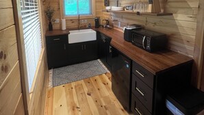 Une cuisine de taille réduite avec des murs en bois et une fenêtre, comprenant un évier, des placards et un four à micro-ondes.