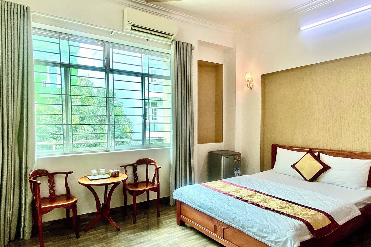 Ein Hotelzimmer mit einem Bett, einem Schreibtisch mit zwei Stühlen, einem Fenster mit Vorhängen und einer Klimaanlage.