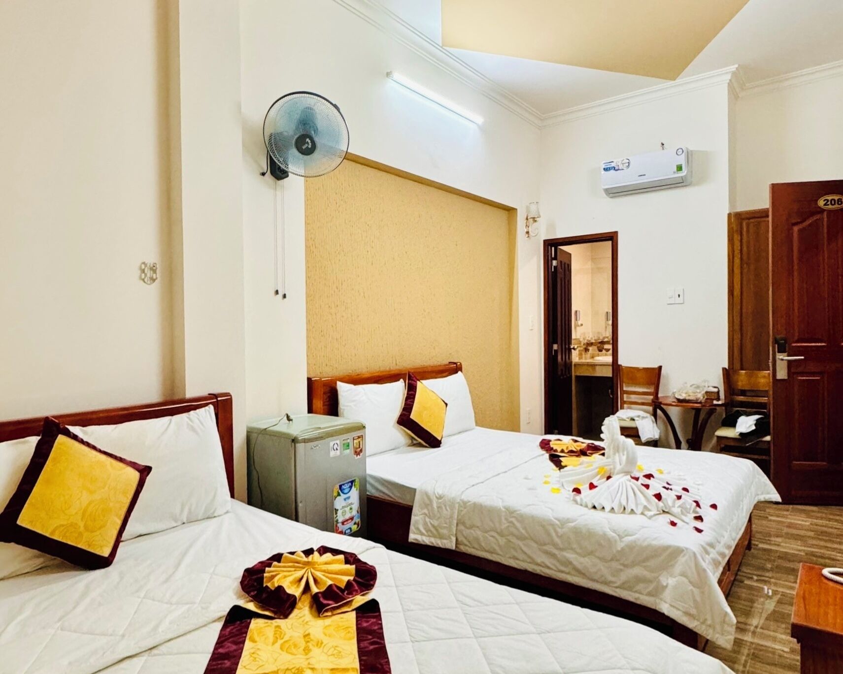A hotel room with two beds, a minibar, an air conditioning unit, and a door leading to a bathroom.