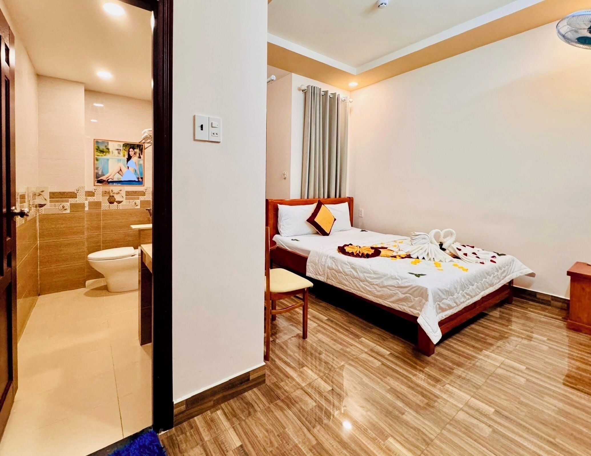 A hotel room with a wooden bed, a bedside table, a bathroom with a toilet and sink, and a shower area.