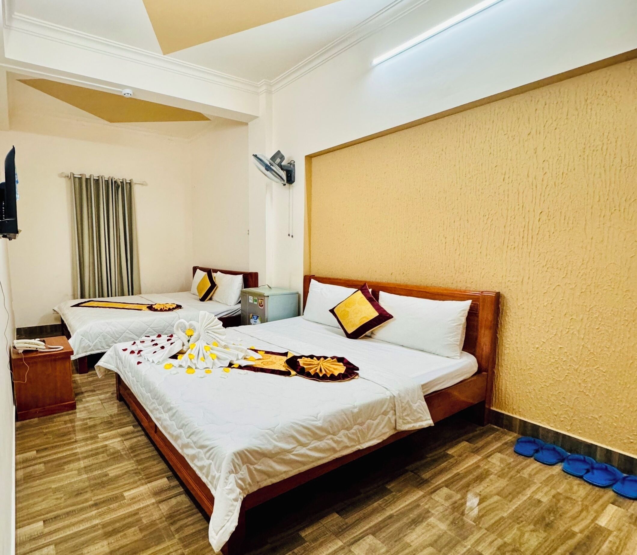 A hotel room with two beds, a wooden headboard, a small bedside table with a phone, a wall-mounted air conditioner, and a curtain.