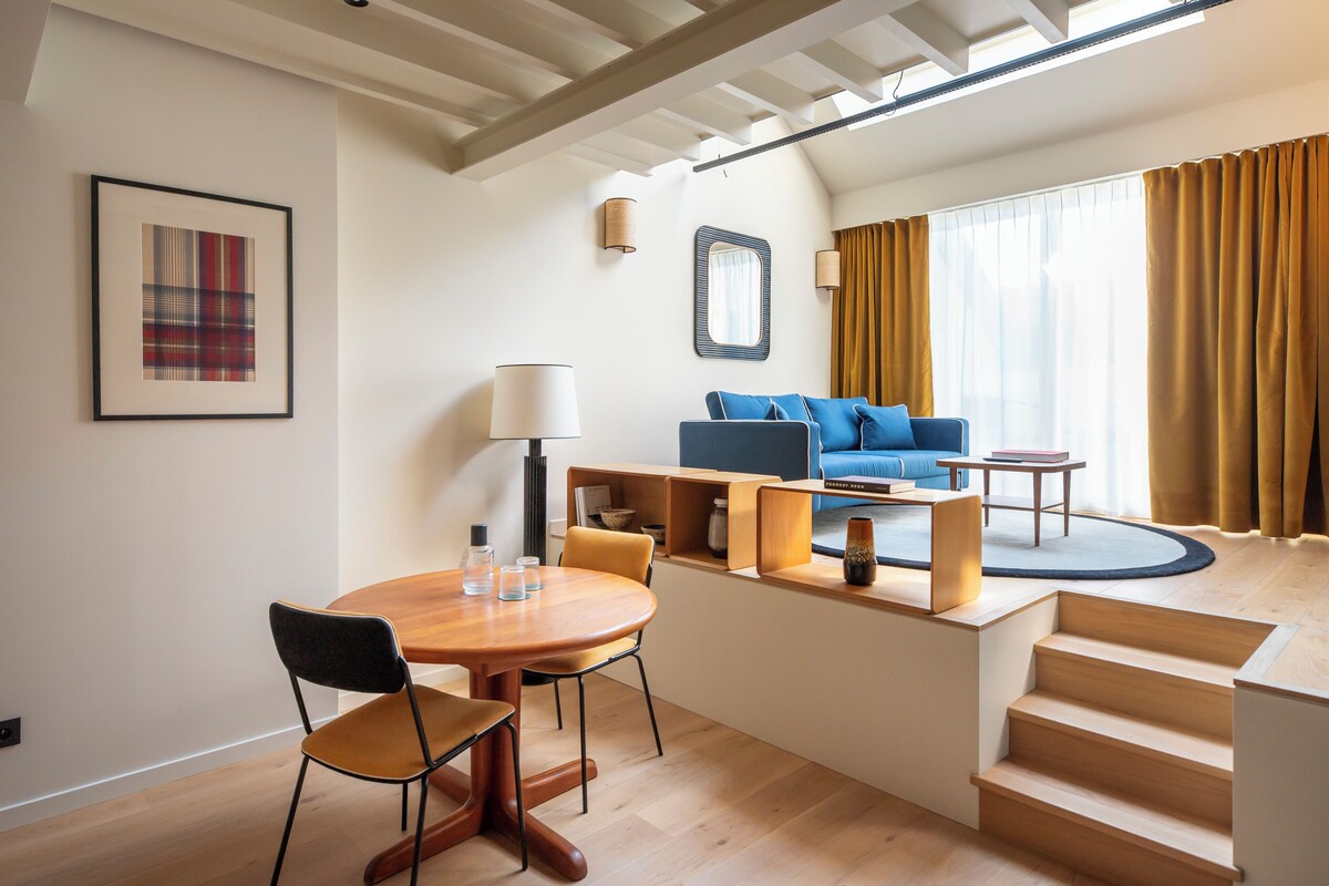 A modern living room with a sofa, coffee table, and a dining area with chairs and a table.
