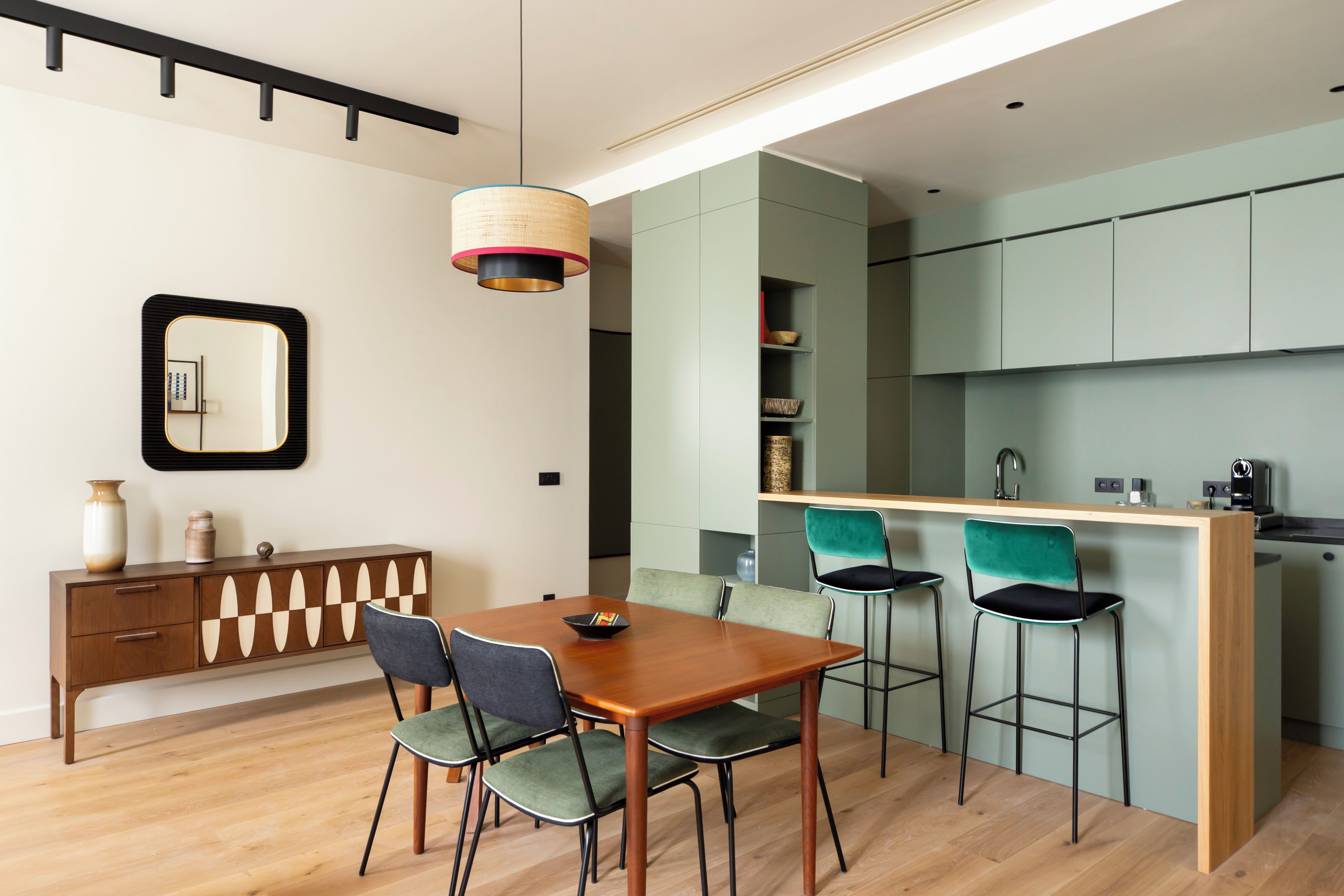 Una cocina moderna con una mesa de comedor de madera y taburetes de bar, una lámpara colgante y un mueble empotrado.
