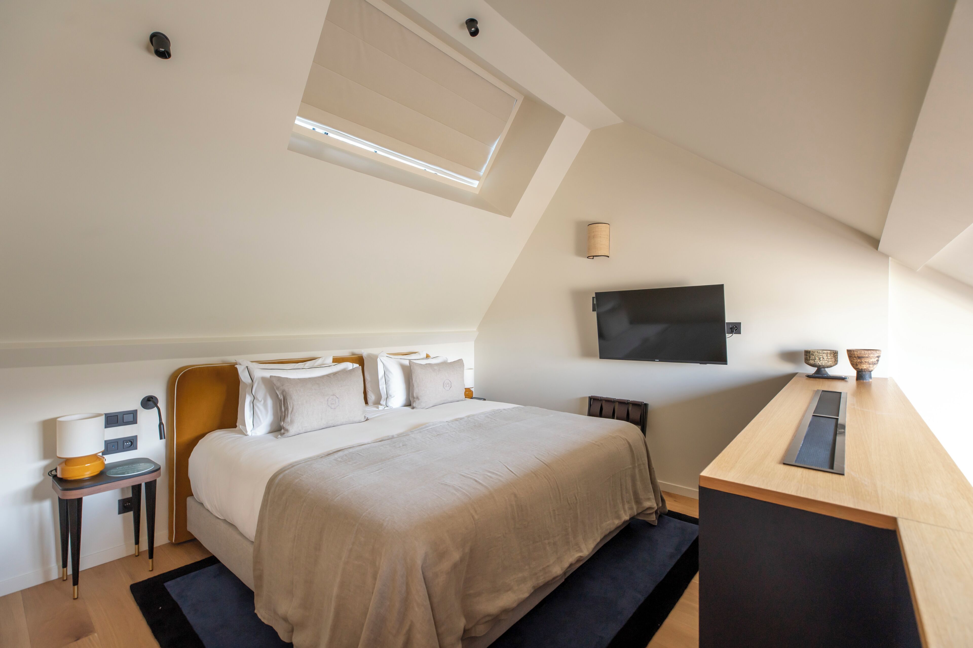 Een slaapkamer met een bed, nachtkastje, lamp en een aan de muur bevestigde televisie.