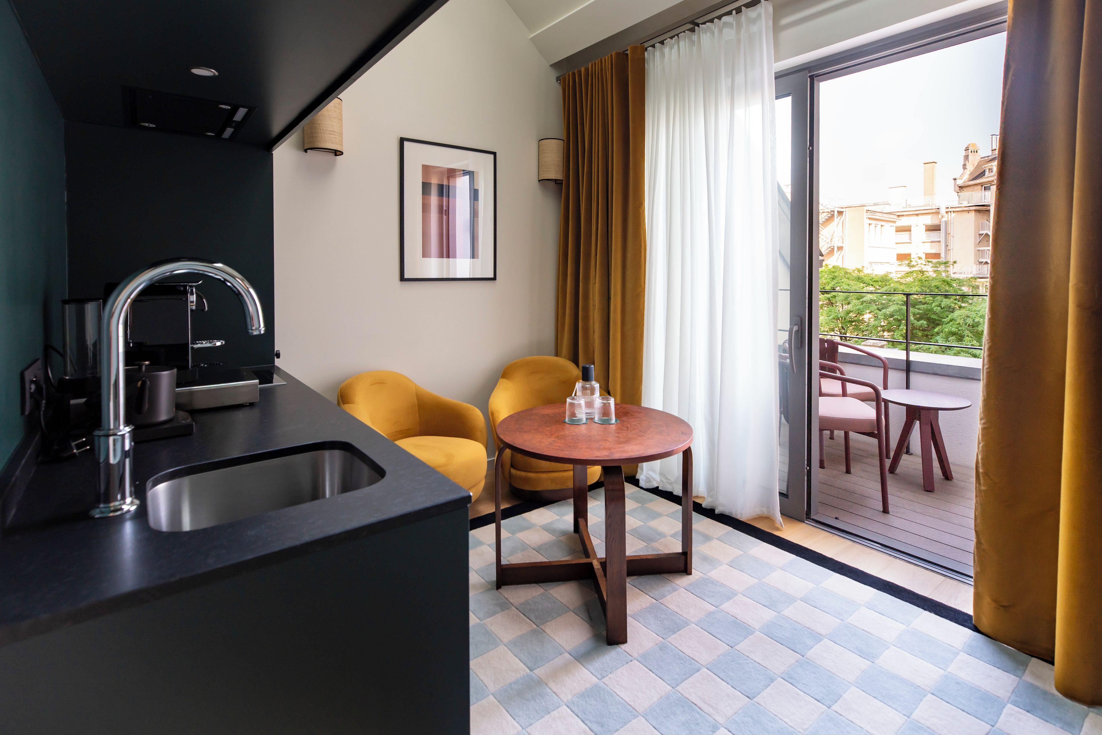Une cuisine compacte dotée d’un évier et d’un robinet modernes, d’une petite table ronde avec deux chaises, et d’une vue sur un balcon aménagé avec des sièges d’extérieur.