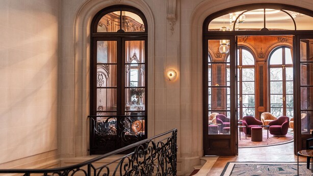 A grand staircase with ornate railings leading to a balcony with plush seating and large windows. - Faubourg 21 – The Leading Hotels of the World (Brussels)