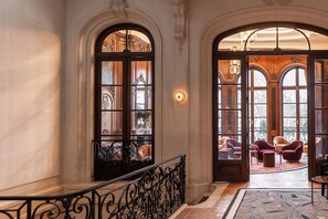 A grand staircase with ornate railings leading to a balcony with plush seating and large windows. - Faubourg 21 – The Leading Hotels of the World (Brussels)