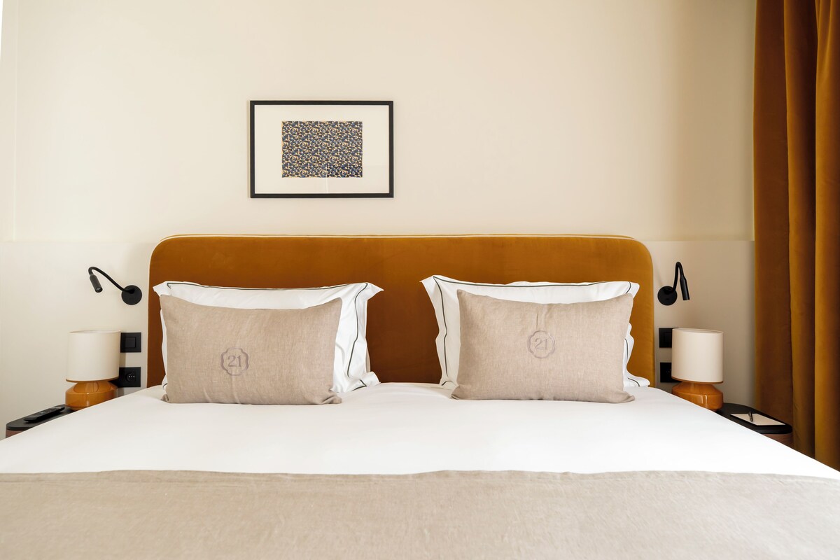 A neatly made bed with two pillows, a headboard, bedside lamps, and a framed picture on the wall.