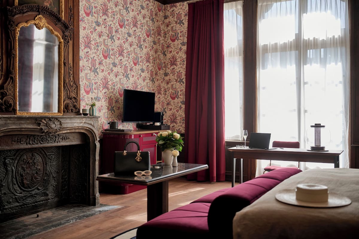 A room with a fireplace, a television, a sofa, and a table with a laptop and a vase of flowers.
