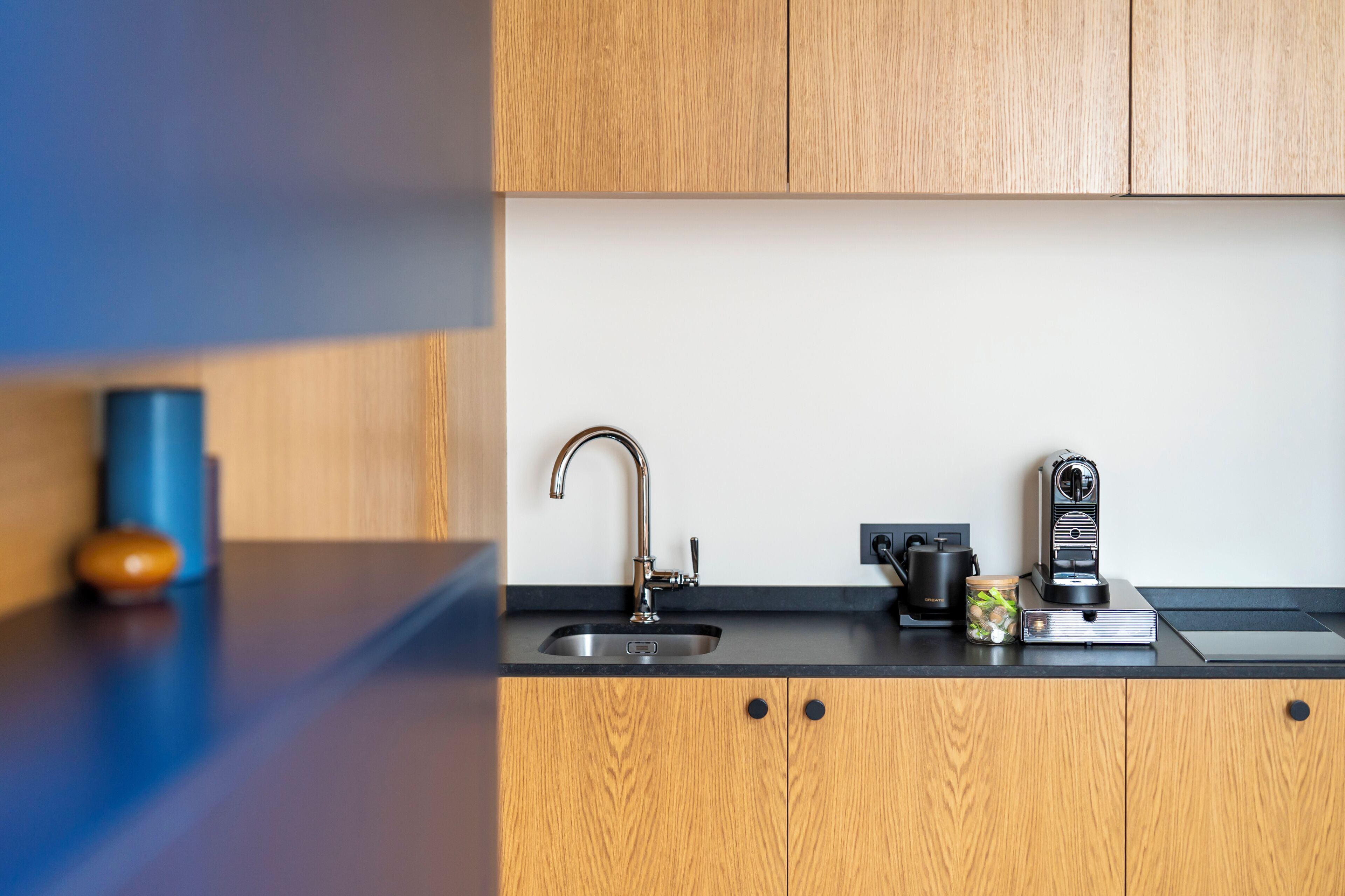 Una cocina moderna con un lavamanos de acero inoxidable, una cafetera y un frasco de ingredientes sobre la encimera.