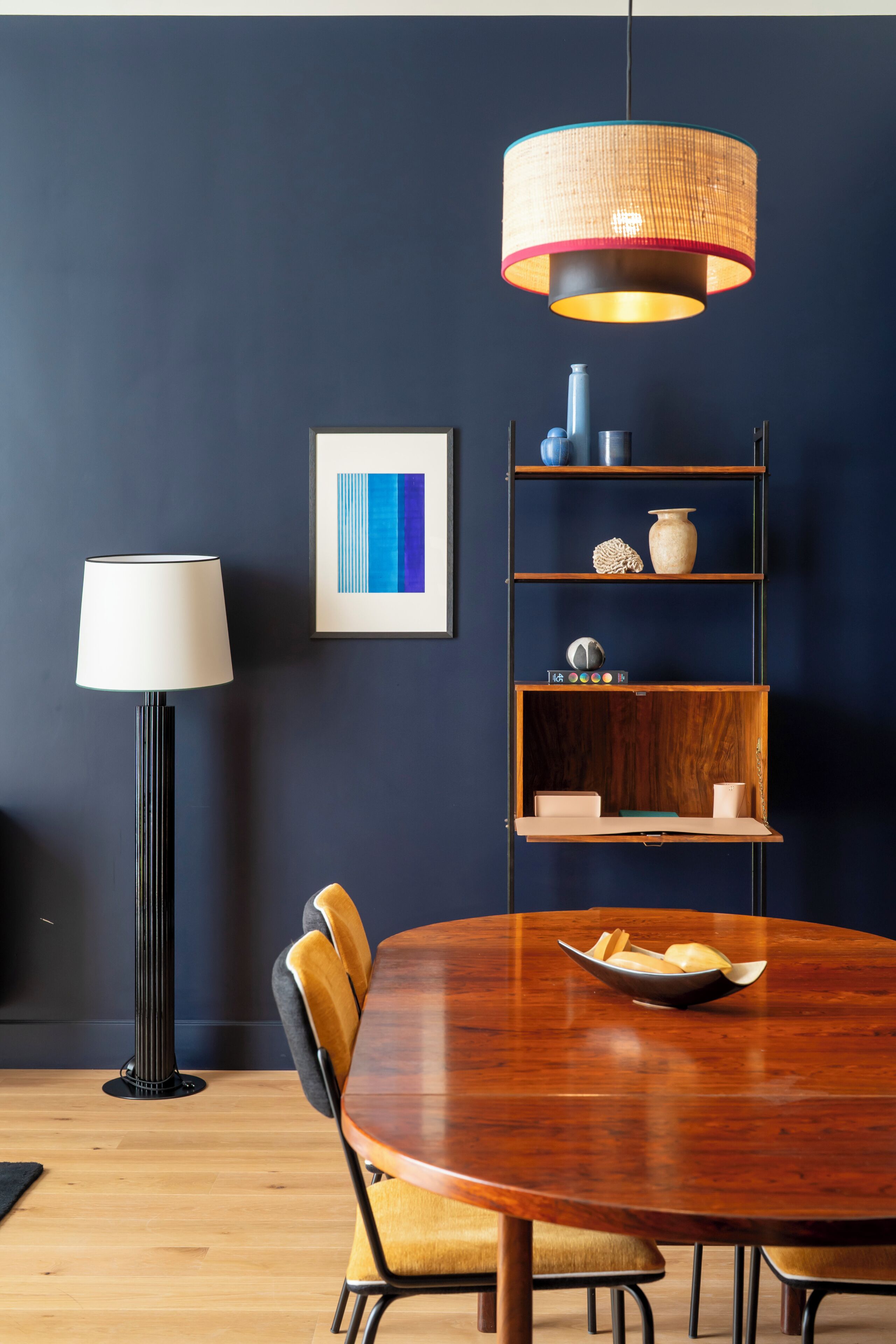 Comedor con una mesa redonda de madera, una lámpara moderna y un estante de pared con objetos decorativos.
