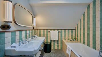 Een badkamer met twee wastafels, een spiegel, een bad en een prullenbak.
