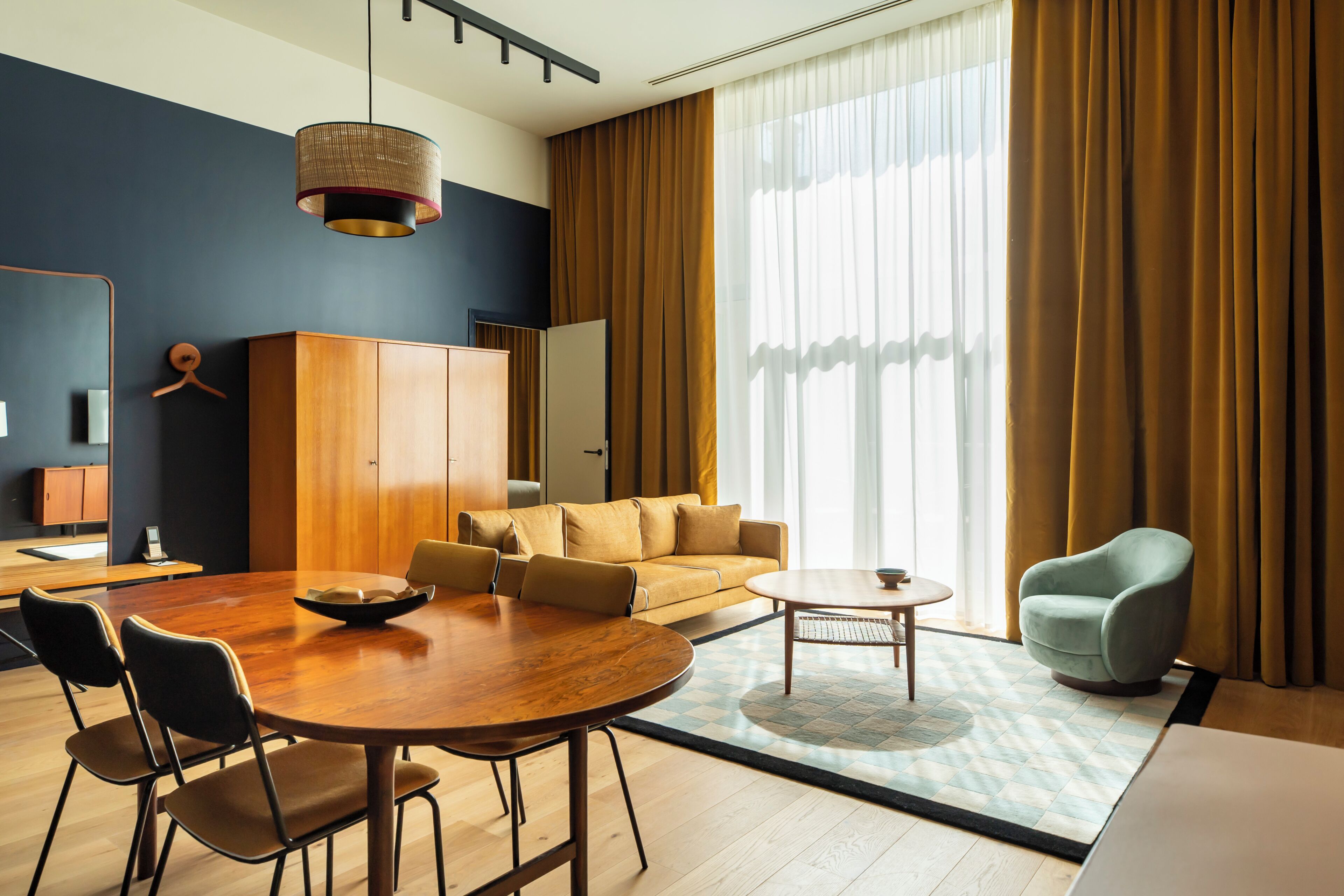 Een moderne hotelkamer met een zithoek, een bank, een stoel en een groot raam met gordijnen.