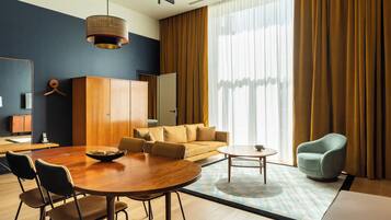 Een moderne hotelkamer met een zithoek, een bank, een stoel en een groot raam met gordijnen.