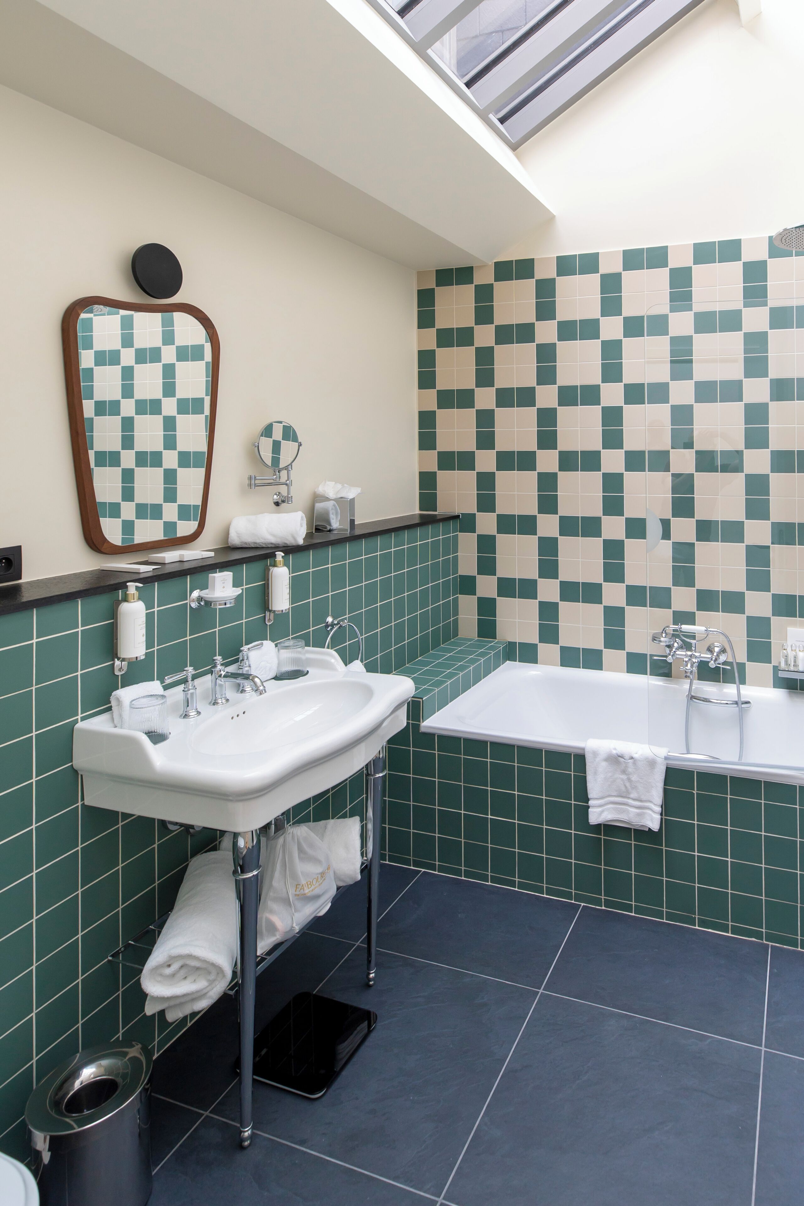 Een badkamer met een betegelde muur in ruitpatroon, een wastafel met spiegel, een badkuip en een toilet.